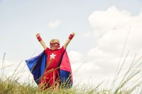 Young Boy dressed as Superhero Raises Arms in Park